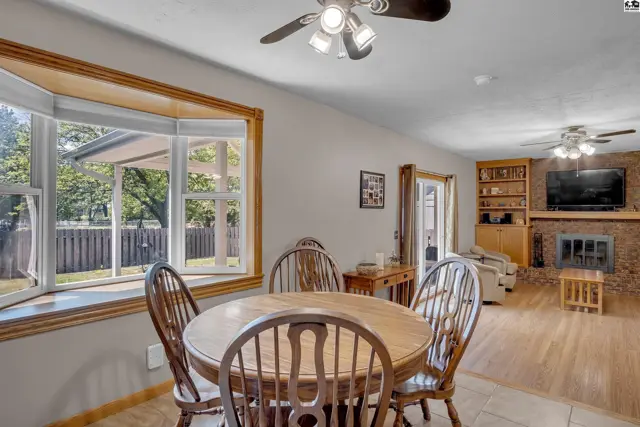Dining area with a bay window and wood table, adjacent to a living room with a brick fireplace.