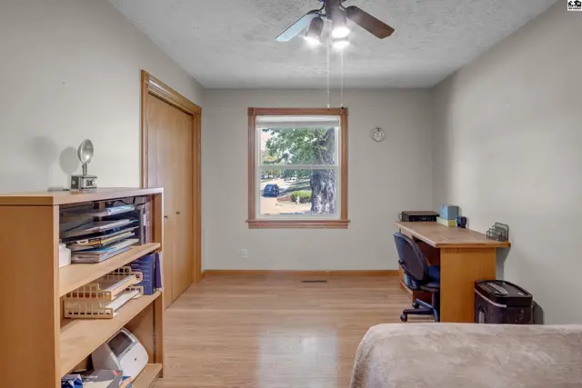 Light-filled bedroom with wood floors, a ceiling fan, and a desk by the window.