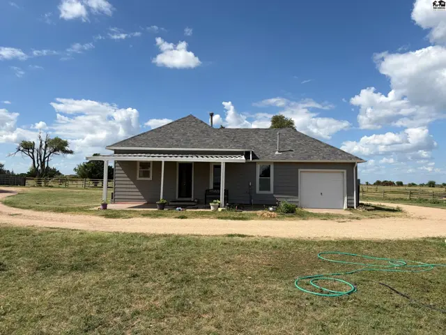 Gray siding ranch home with a covered porch, attached garage, and gravel driveway on a sunny day.