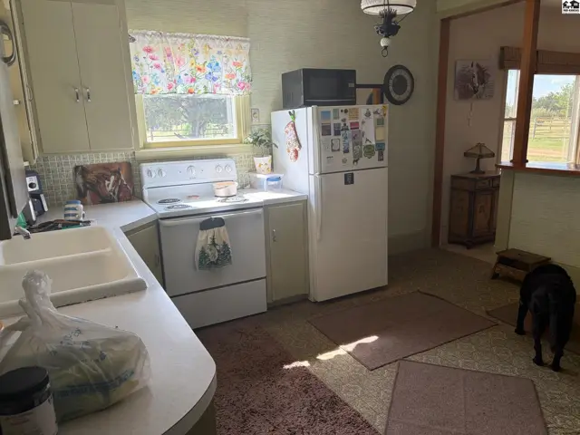 A vintage kitchen with white appliances, floral curtains, and light green walls.
