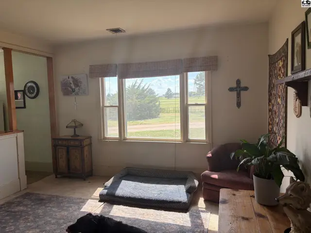 Living room with large window, armchair, and dog bed, featuring rustic decor and natural light.