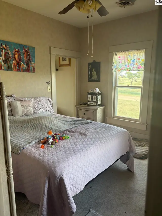 Cozy bedroom with a queen bed, patterned bedding, and a window overlooking a rural landscape.