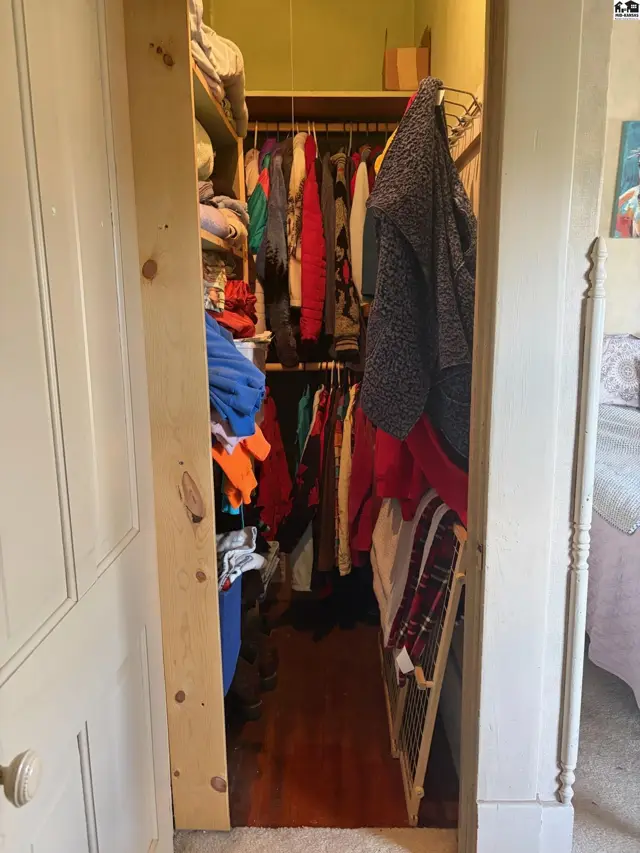 Spacious walk-in closet with wood floors, shelves, and hanging rods filled with clothing.