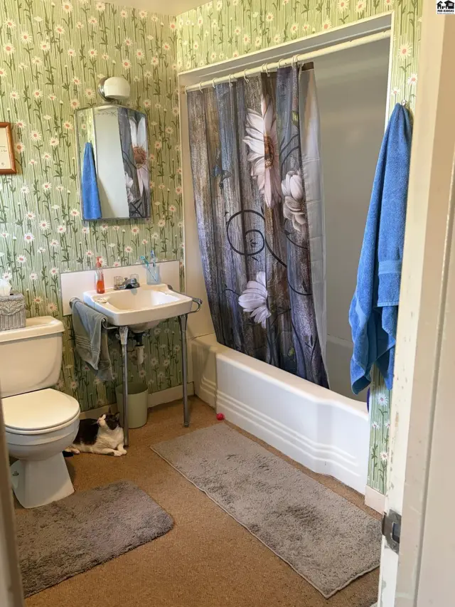 Charming bathroom with floral wallpaper, pedestal sink, white tub, and a rustic shower curtain.