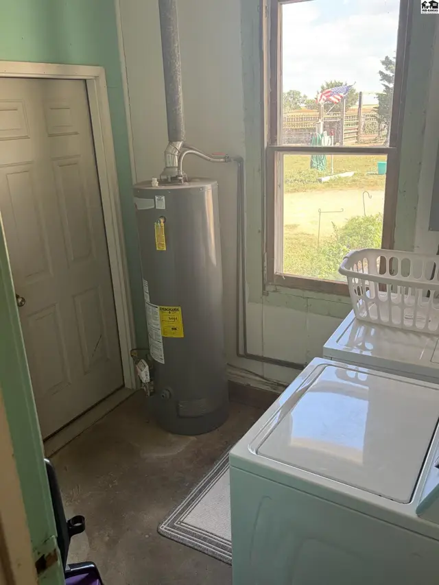 Laundry room with a water heater, washing machine, and a window overlooking the exterior.