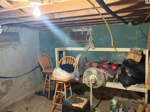 Unfinished basement with concrete walls, exposed joists, and storage items.