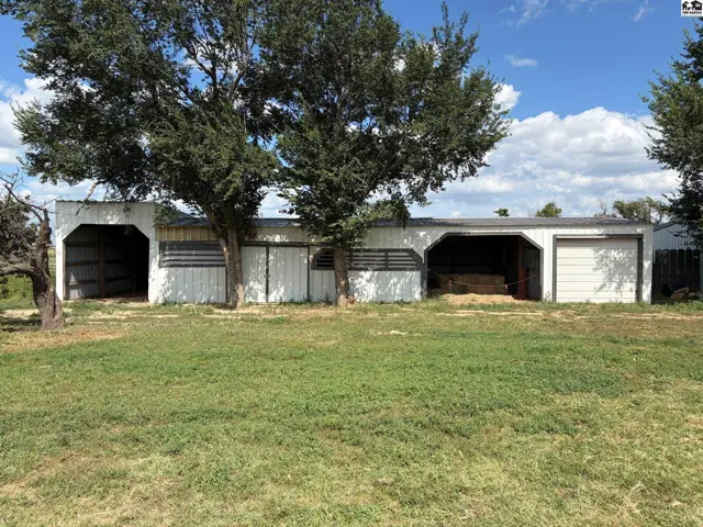 White barn with open stalls and garage doors, set against a grassy yard and blue sky.