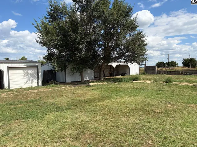 White sided home with attached carport and detached garage sits on a grassy lot.