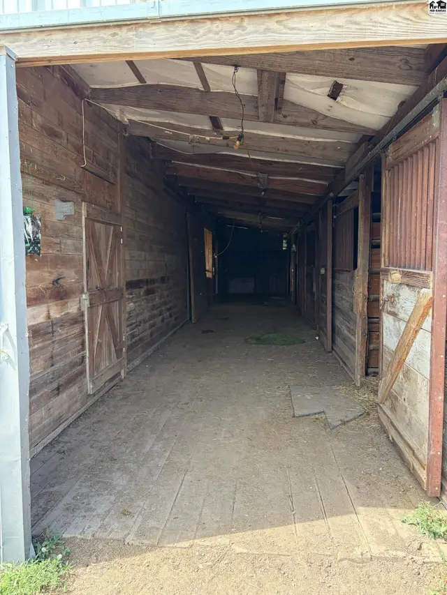 Rustic wooden barn aisle with stalls, featuring weathered wood and a dirt floor.