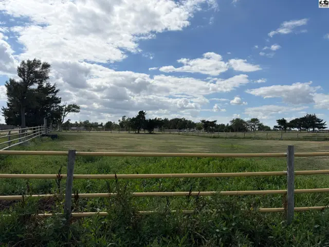 Expansive green pasture with a yellow metal fence under a bright, cloudy sky.