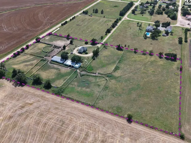 Aerial view of a sprawling rural property with a house, stables, pastures, and a pool.