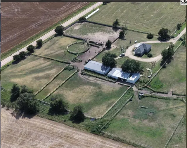 Aerial view of a ranch property with a house, barn, stables, and fenced pastures.