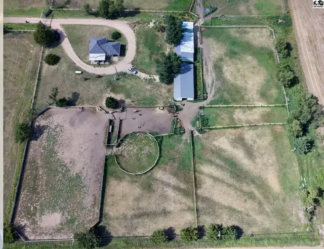 Aerial view of a rural property featuring a house, barns, and horse riding arenas.