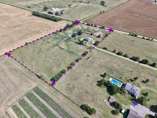 Aerial view of a sprawling rural property with a house, pool, and fenced acreage.
