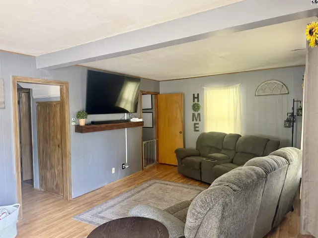 Living room with gray walls, wood floors, a large TV, and comfortable green recliners.