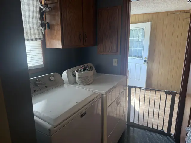 Laundry room with white washer and dryer, wood cabinets, and a white door.