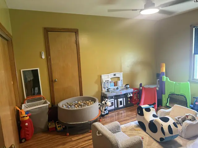 Bright playroom with ball pit, toy kitchen, and child-sized furniture on hardwood floors.