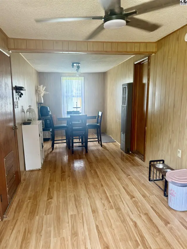 Dining area with wood-paneled walls, laminate flooring, and a ceiling fan.