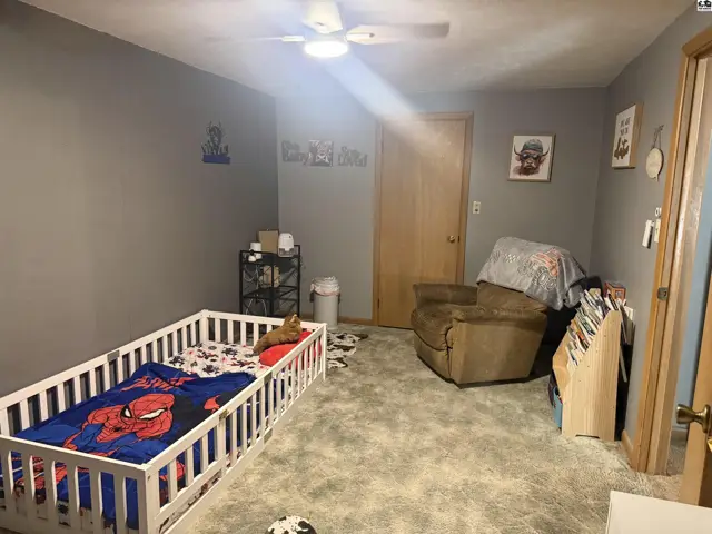 A child's bedroom with a toddler bed, recliner, and gray carpet.