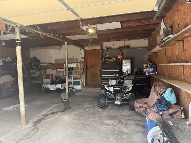 Spacious garage with concrete floor, wood-paneled walls, and storage shelves, featuring an ATV and children's ride-on toy.