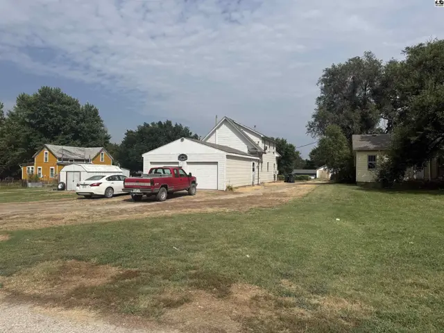 White house and garage with red truck and cars parked on a grassy lot.