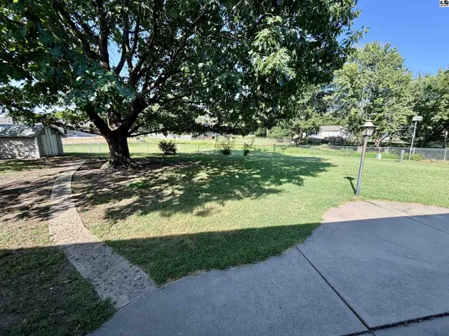 Spacious backyard with mature tree, paved path, and a small shed.
