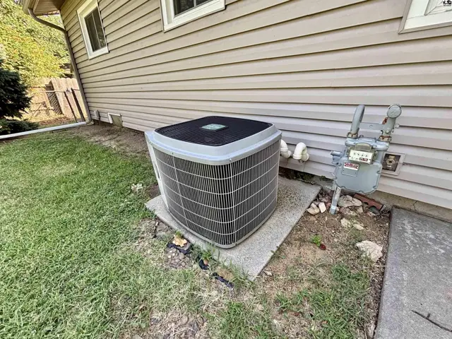 Exterior view of a tan vinyl-sided house with an air conditioning unit and gas meter.