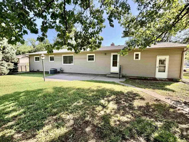 Backyard view of a tan vinyl-sided ranch home with a concrete patio and mature trees.