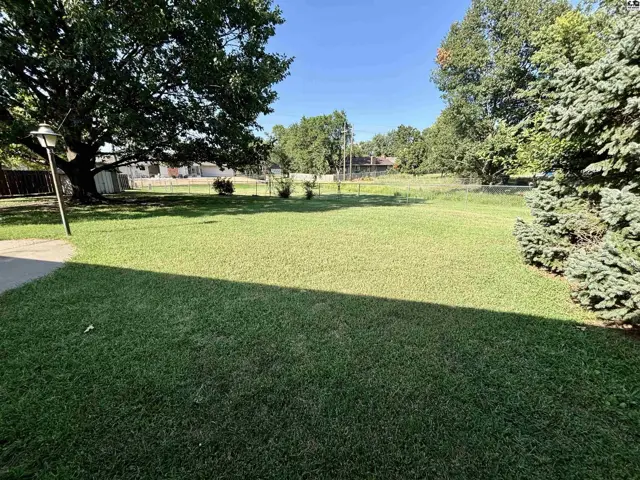 Spacious, manicured green lawn with mature trees and a lamp post under a clear blue sky.