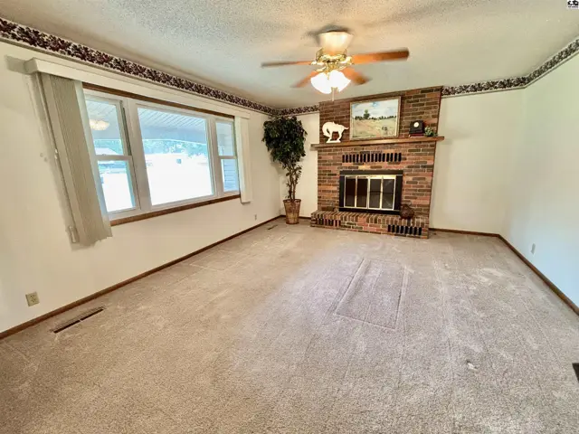 Spacious living room with a brick fireplace, large windows, and neutral carpet.