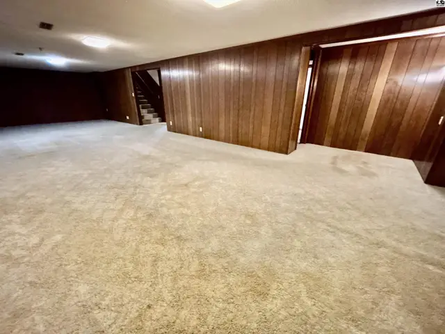 Spacious basement with plush carpet and warm wood-paneled walls, featuring a staircase.