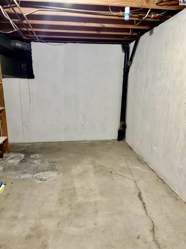 Unfinished basement with concrete floor, white-plastered walls, and exposed wooden ceiling joists.