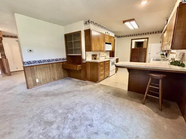 Spacious kitchen with wood cabinetry, white appliances, and a breakfast bar with a stool.