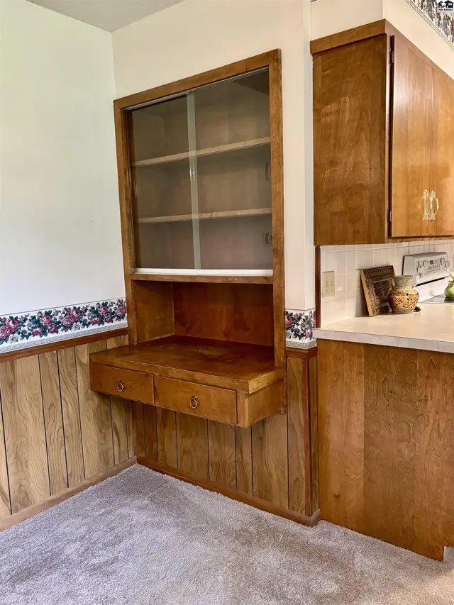 Built-in wooden hutch with glass doors and drawers above paneled walls and floral wallpaper.