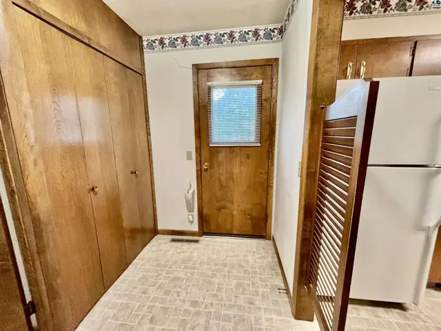 Wood-paneled closets and a door with a window accent this hallway with a white refrigerator.
