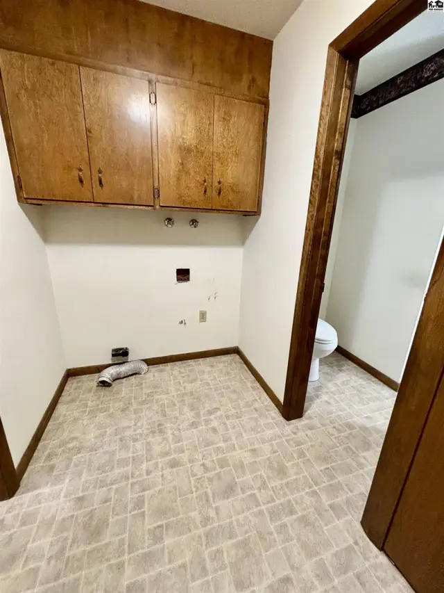 Laundry room with wood cabinets, vinyl flooring, and a glimpse of a toilet in an adjacent room.