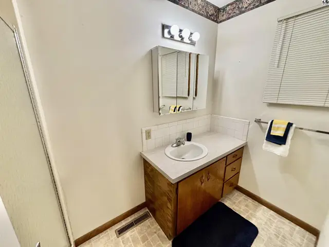Bathroom with a white vanity, wood cabinets, tiled backsplash, and a patterned wallpaper border.