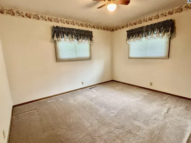 Neutral carpeted bedroom with two windows, floral wallpaper border, and ceiling fan.