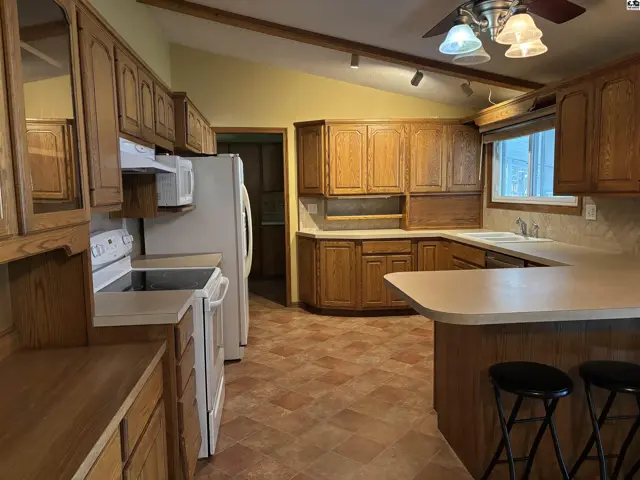 Spacious kitchen with oak cabinets, white appliances, and a breakfast bar.