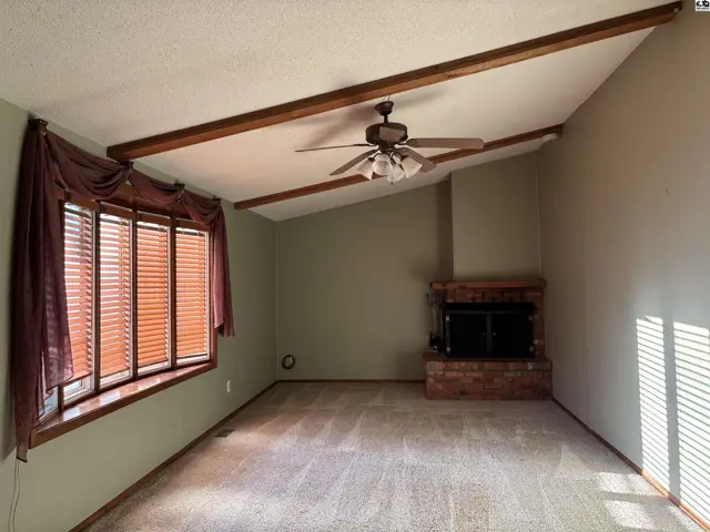 Living room with vaulted ceiling, exposed beams, large bay window, and brick fireplace.