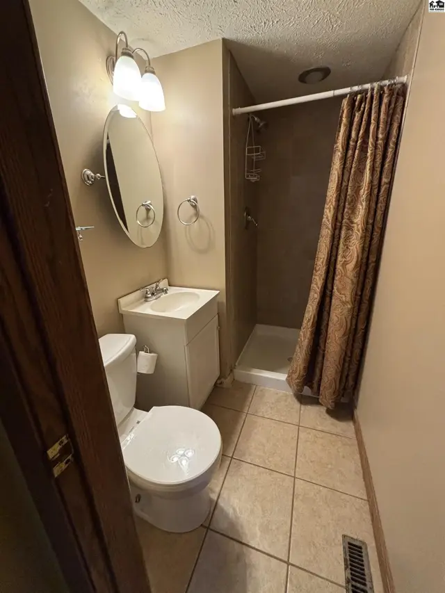 Compact bathroom with a white vanity, oval mirror, and a shower with a patterned curtain.