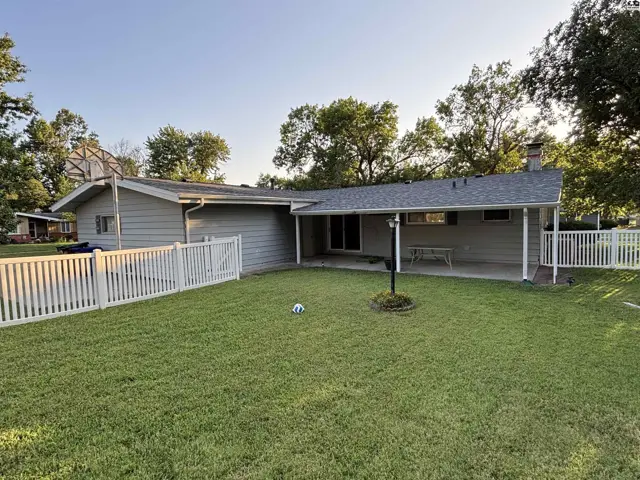 Spacious backyard with a white picket fence, covered patio, and mature trees.
