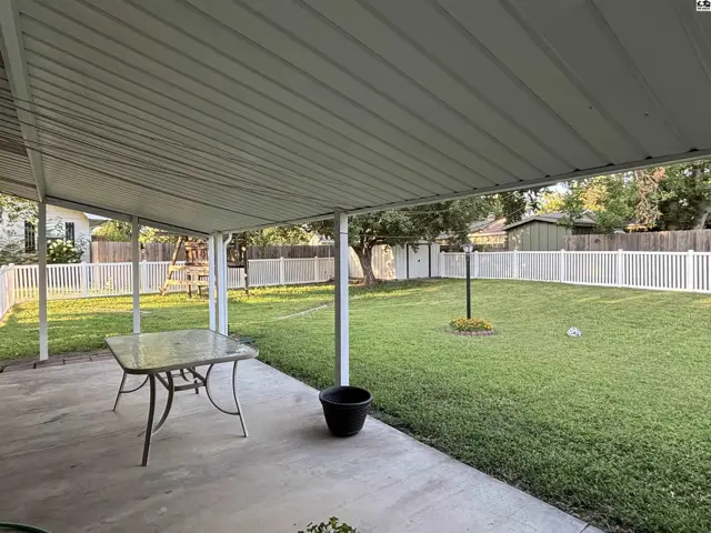 Covered patio overlooks a fenced backyard with a picnic table and mature trees.
