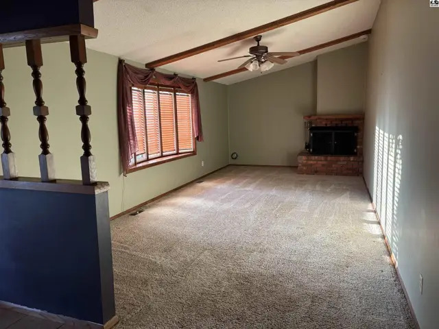 Spacious living room with vaulted beamed ceiling, brick fireplace, and large window.