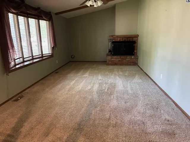 Spacious living room with a brick fireplace, bay window, and neutral carpet.