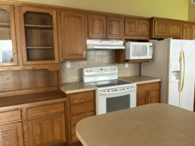 Spacious kitchen with oak cabinetry, white appliances, and a tiled backsplash.