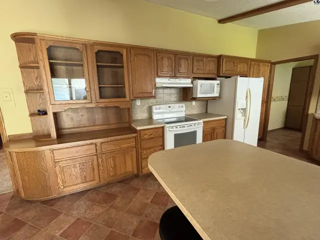 Kitchen with light oak cabinetry, tiled backsplash, white appliances, and a large island.