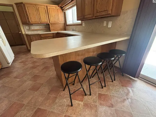 Kitchen with light oak cabinets, a large laminate countertop with seating, and tiled flooring.