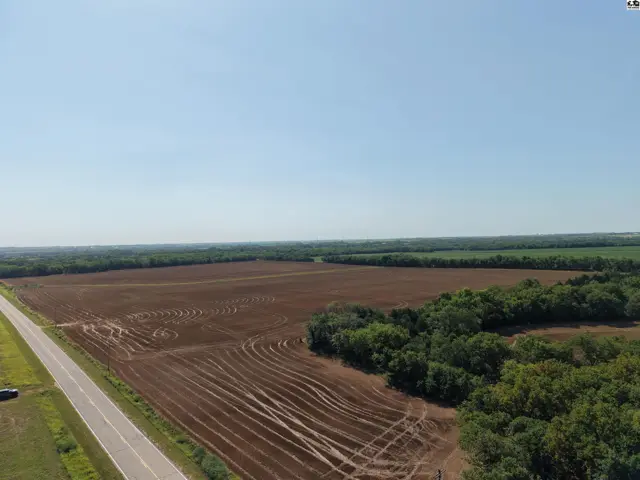 Expansive agricultural field with tilled soil and tree line under a clear blue sky.