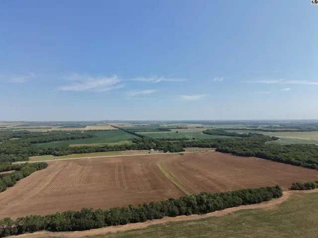 Expansive aerial view of cultivated fields and wooded areas under a clear blue sky.